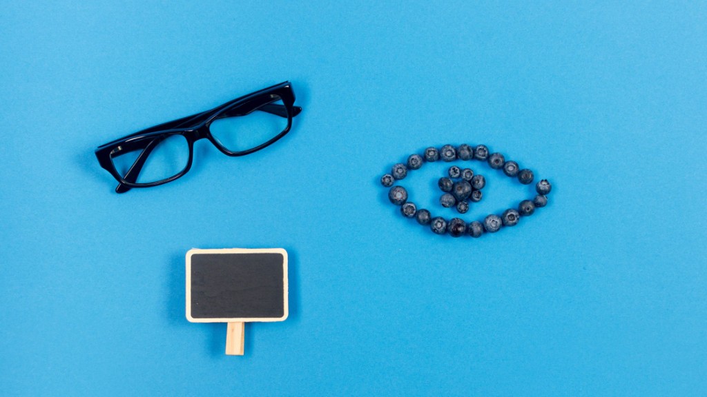 Eyeglasses, blueberries arranged like an eye, and a small chalkboard on a blue background